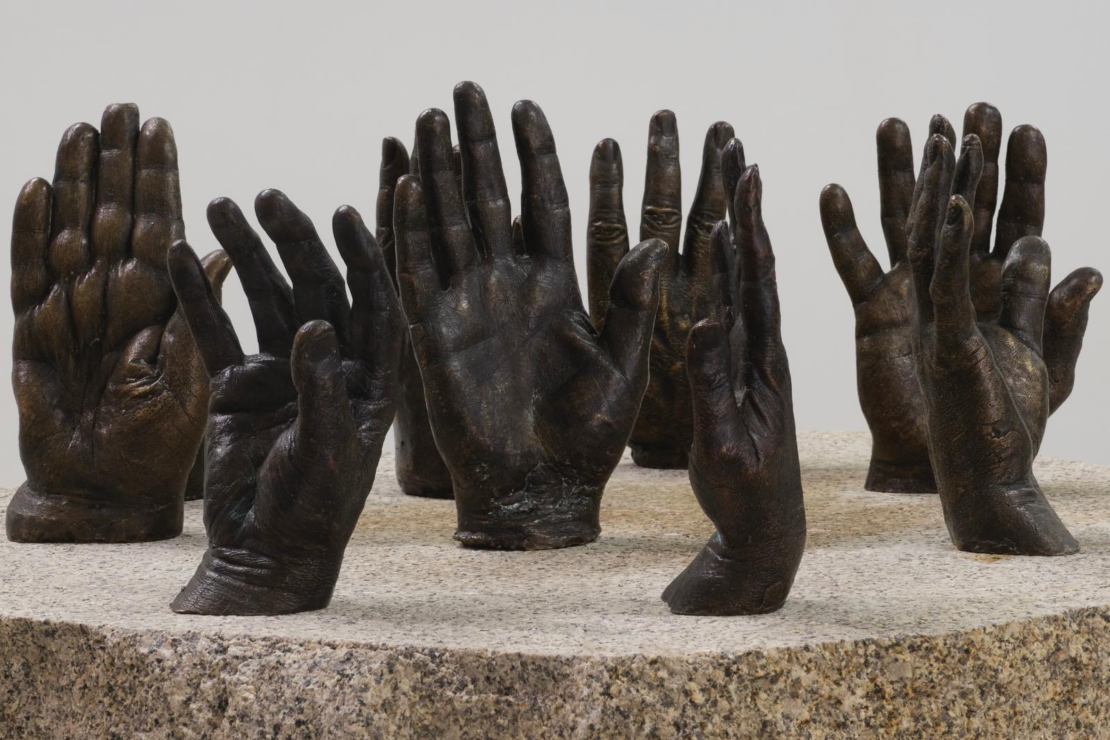 Installation shot of Raymond Watson's work 'Hands of History'. Assortment of bronze cast hands arrange on a stone plinth.